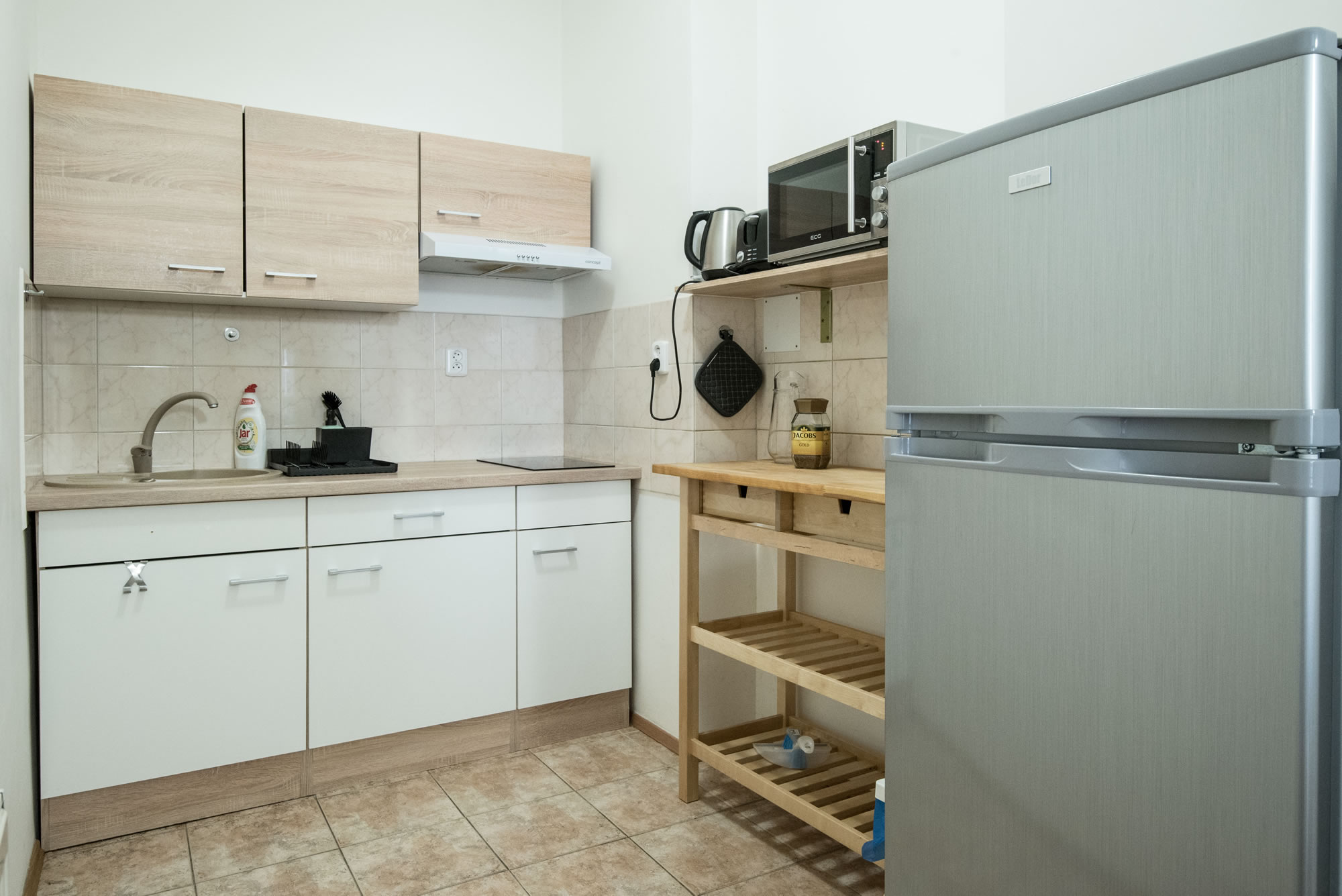 Kitchen with microwave and a fridge. Tiles are on the floor