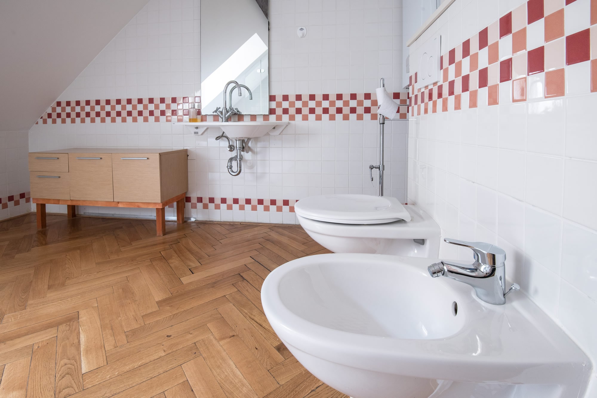 Large bathroom covered by white tiles and wooden parquet.