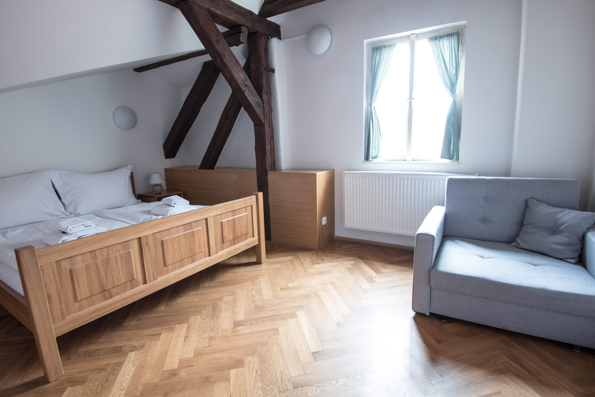 Bedroom in the attic apartment. Wooden bed, wooden floor and small grey sofa chair
