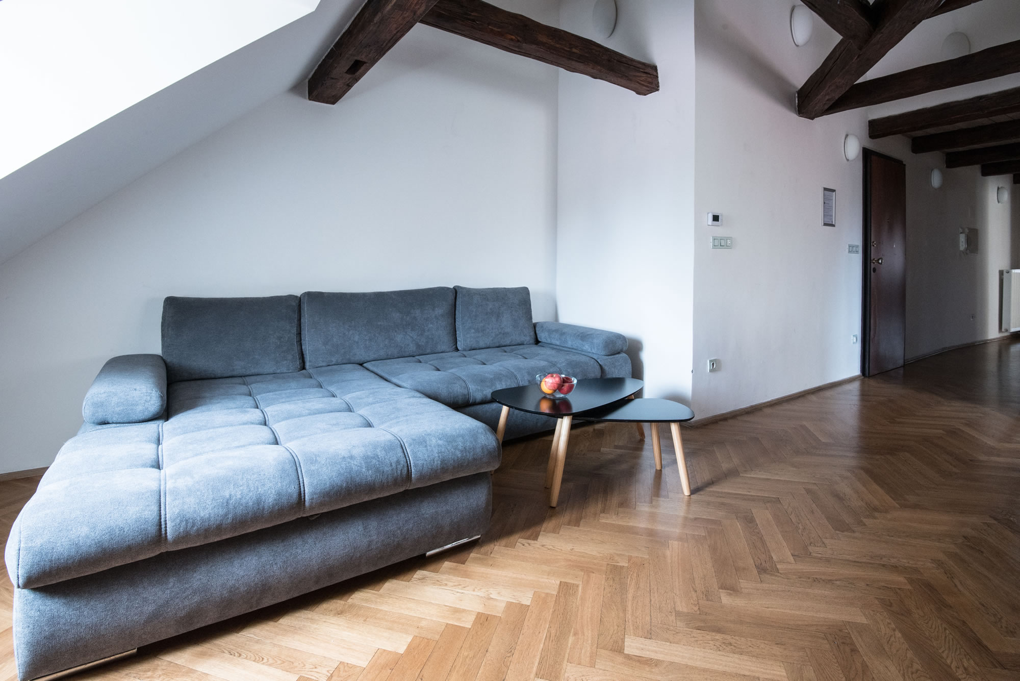 Large attic apartment with wooden beams. A grey sofa with black coffee table dominates the room.