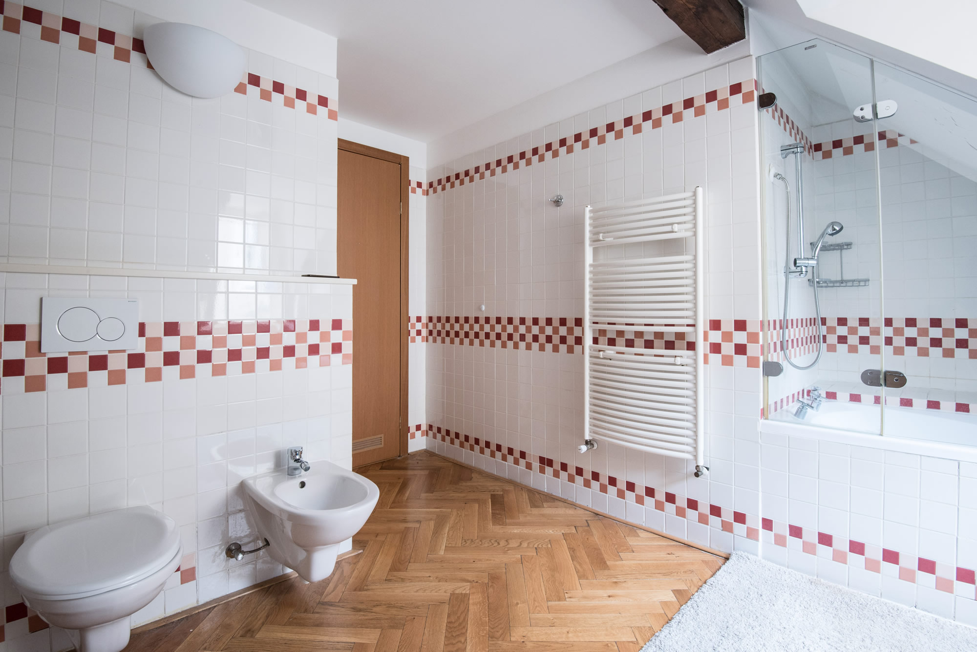 Large bathroom with wooden parquet covered with white tiles. There is a bath tube, toilet and bidet.