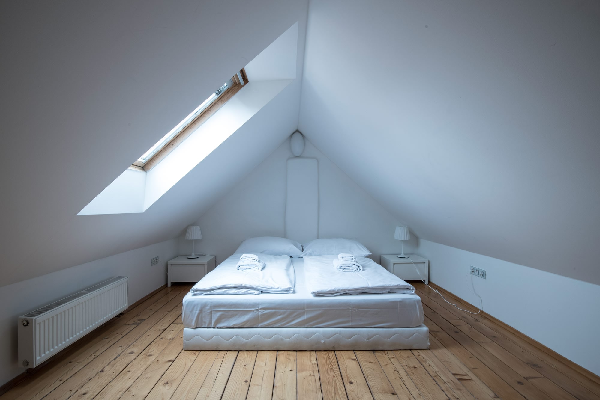 Attic bedroom with queen sized bed and wooden floor.