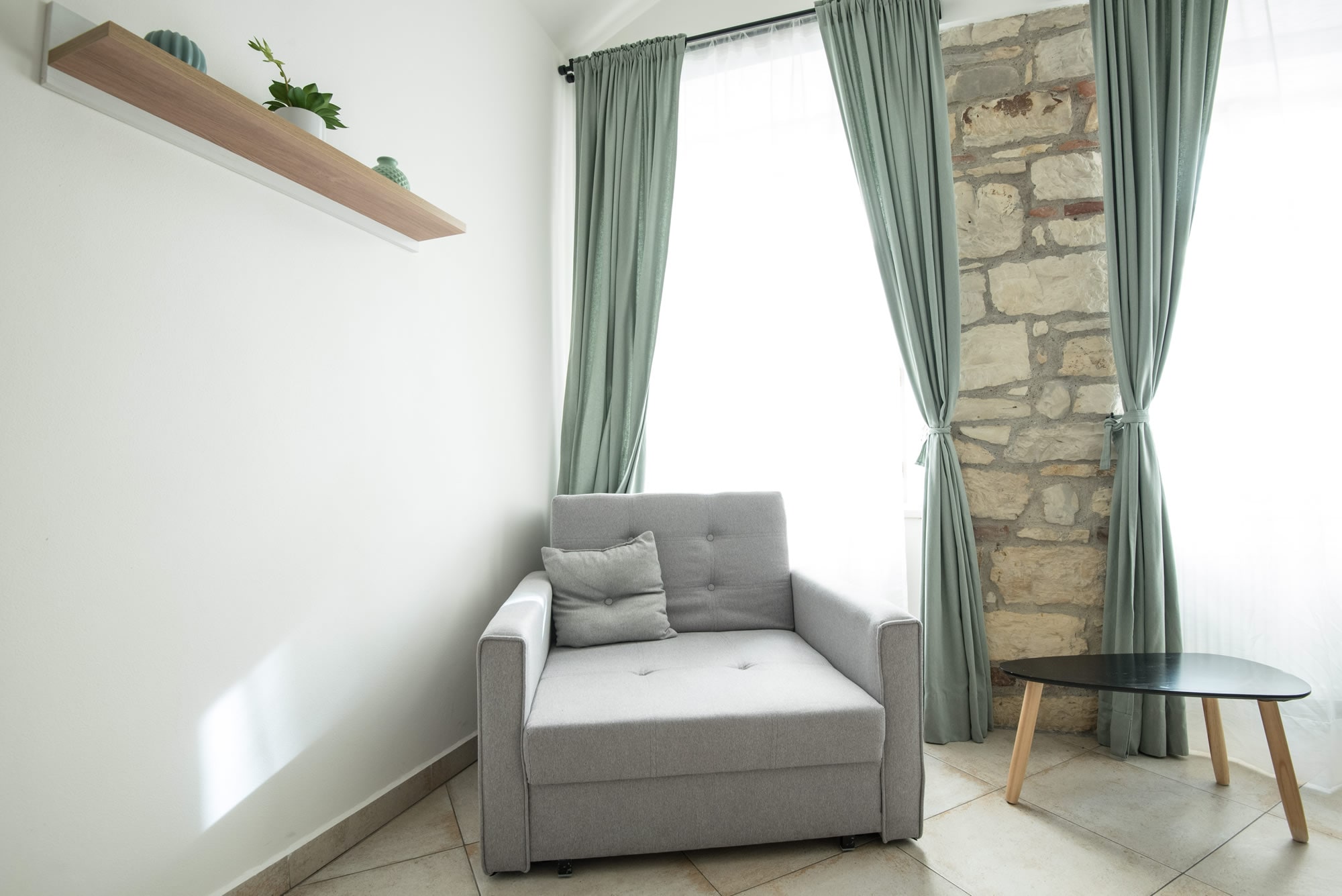 Sofa chair near large window and stone wall