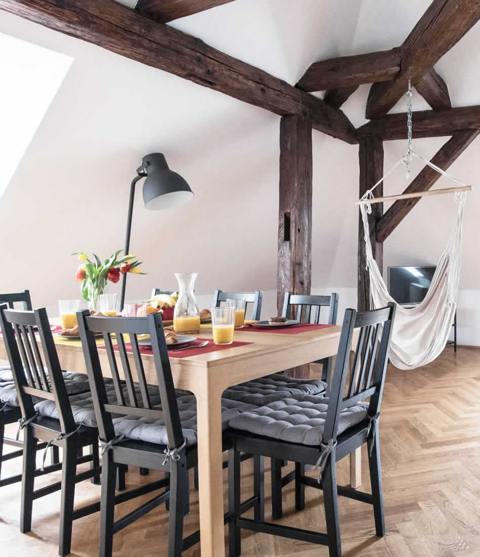 Dining table in the middle of large living room with breakfast served. Wooden beams dominate the room